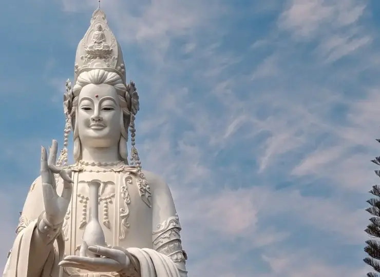 White Buddha statue rising against a cloudy blue sky