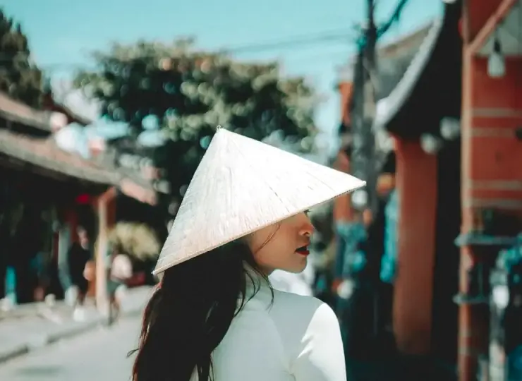 Woman wearing a white nón lá walking along a street in Vietnam