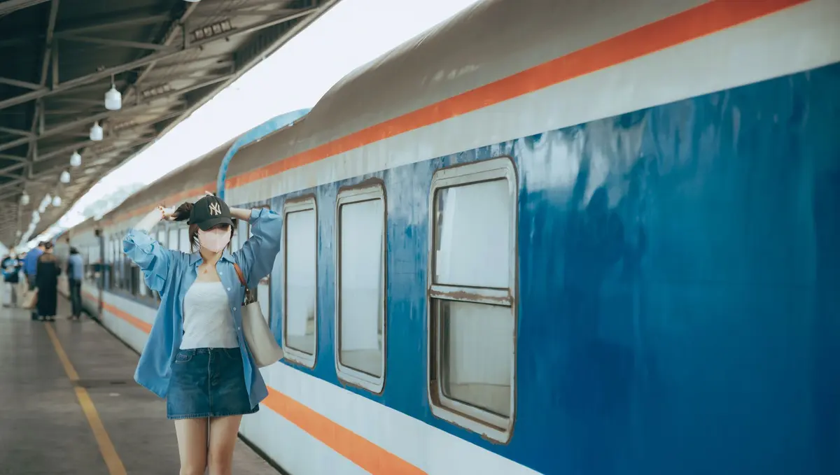 Traveler standing beside a blue passenger train at a Vietnamese railway station