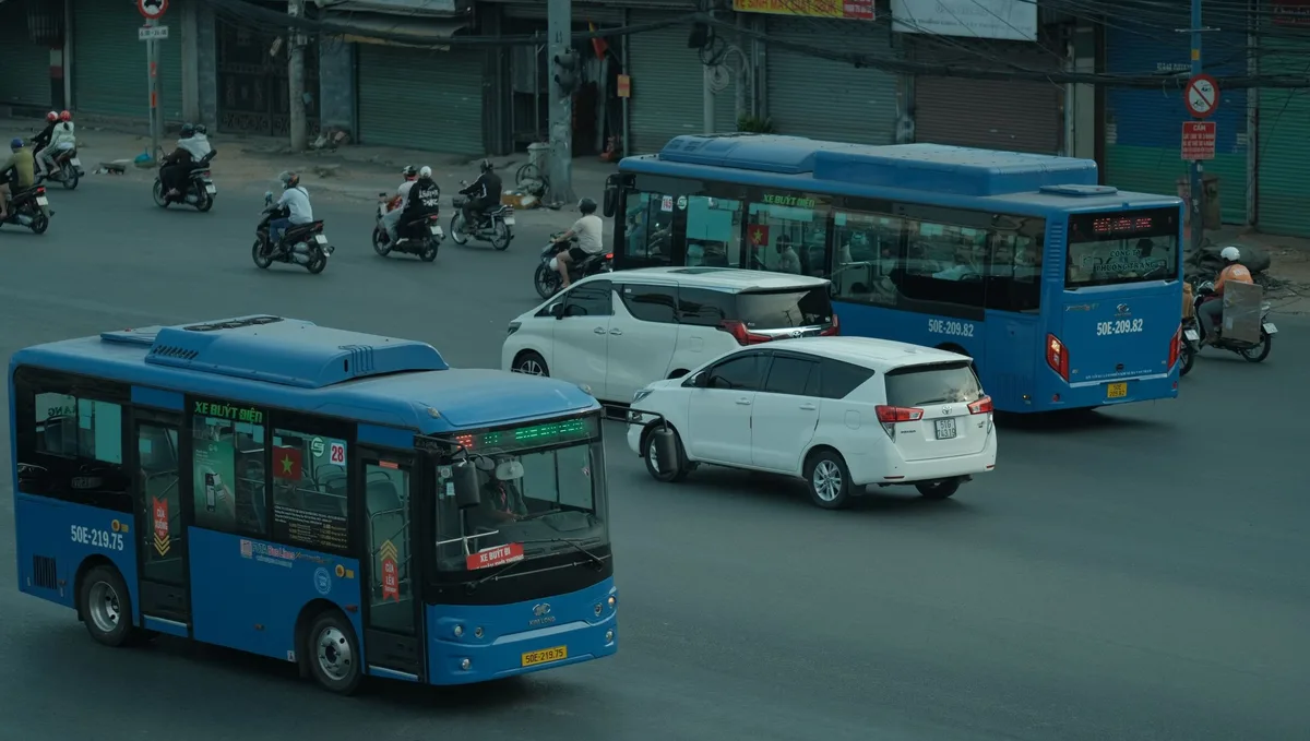 Two blue city buses and cars crossing a wide junction in Ho Chi Minh City
