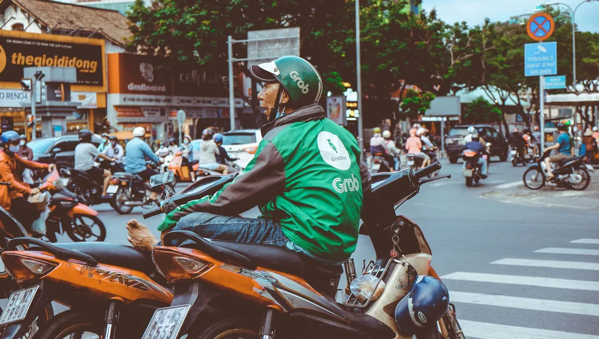 Grab motorbike driver in a green jacket and branded helmet waiting in traffic in Ho Chi Minh City