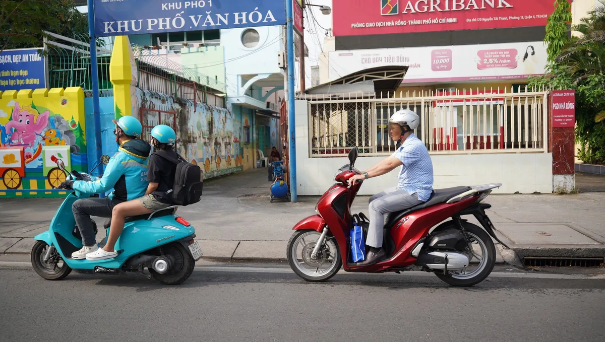 Turquoise Xanh SM electric motorbike taxi carrying a passenger past a private rider in Ho Chi Minh City
